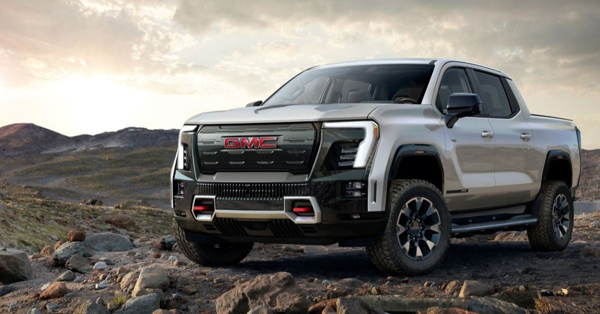 2026 GMC Sierra EV pickup truck parked on rugged terrain at sunset, highlighting its off-road capability and bold front design.