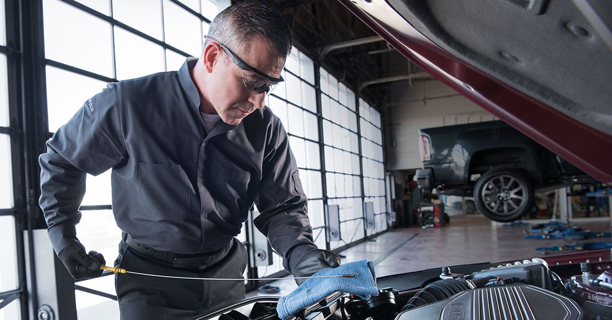 Mechanic under hood looking for low oil symptoms.